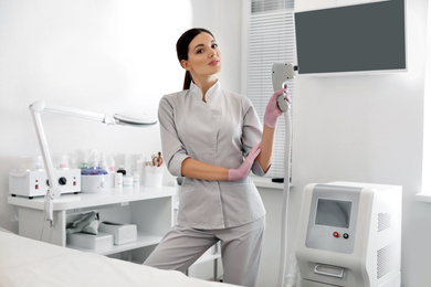 Photo of Young woman holding professional laser epilator in beauty salon