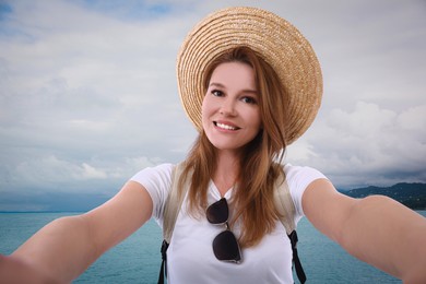 Beautiful woman in straw hat taking selfie near sea