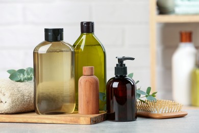Photo of Shampoo bottles, hair brush, towel and leaves on light grey table