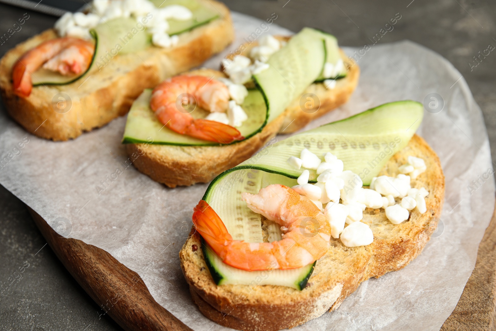 Photo of Cutting board of delicious bruschettas with shrimps on grey table, closeup