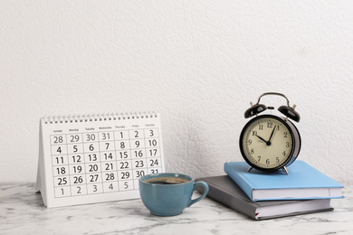Photo of Composition with calendar, cup of coffee and notebooks on white marble table