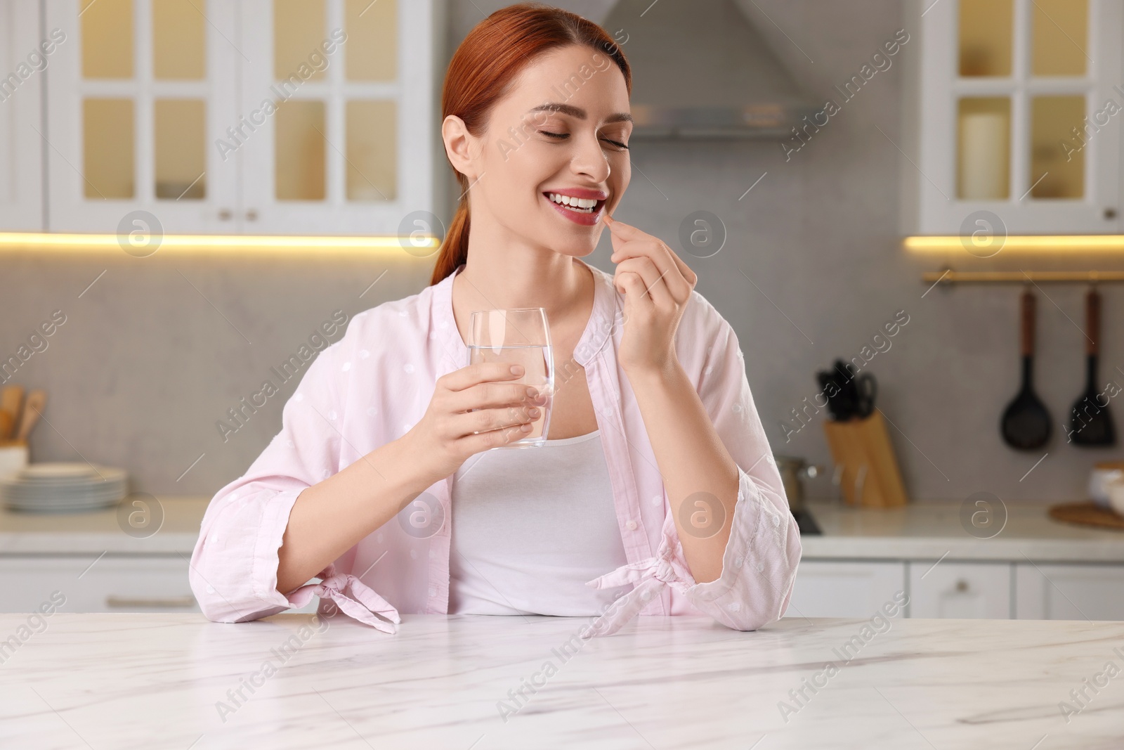 Photo of Beautiful young woman taking vitamin pill at home