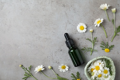 Flat lay composition with bottle of essential oil and flowers on table, space for text