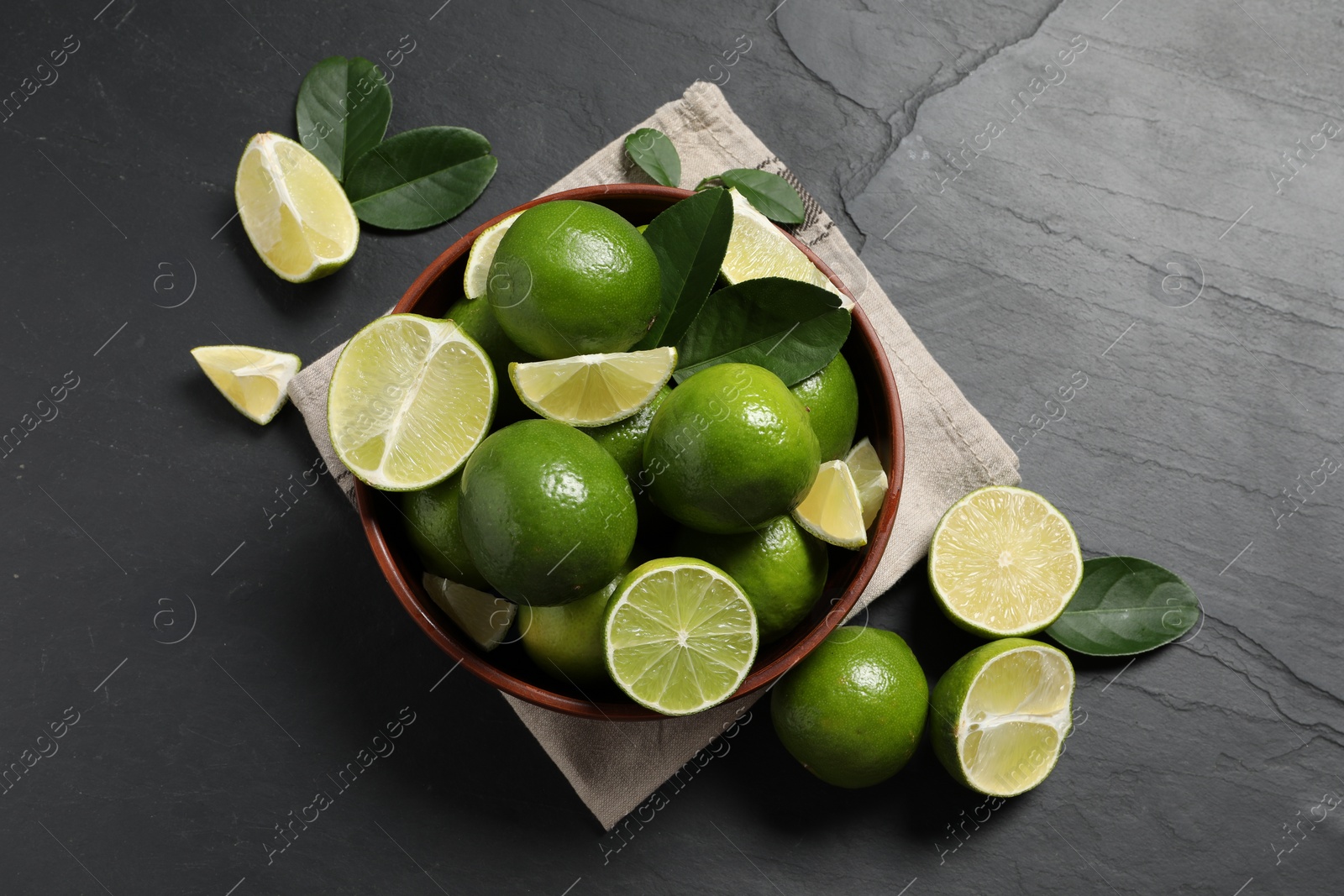 Photo of Fresh ripe limes in bowl on black table, top view