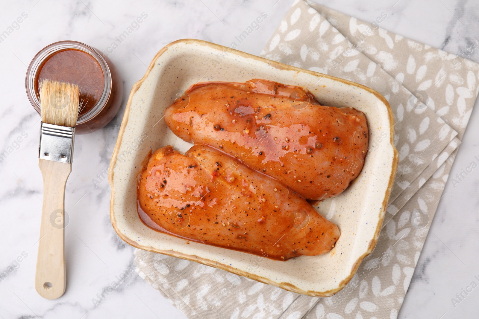 Photo of Raw marinated chicken fillets and basting brush on white marble table, flat lay