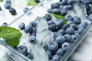 Photo of Juicy blueberries with green leaves and ice on table, closeup