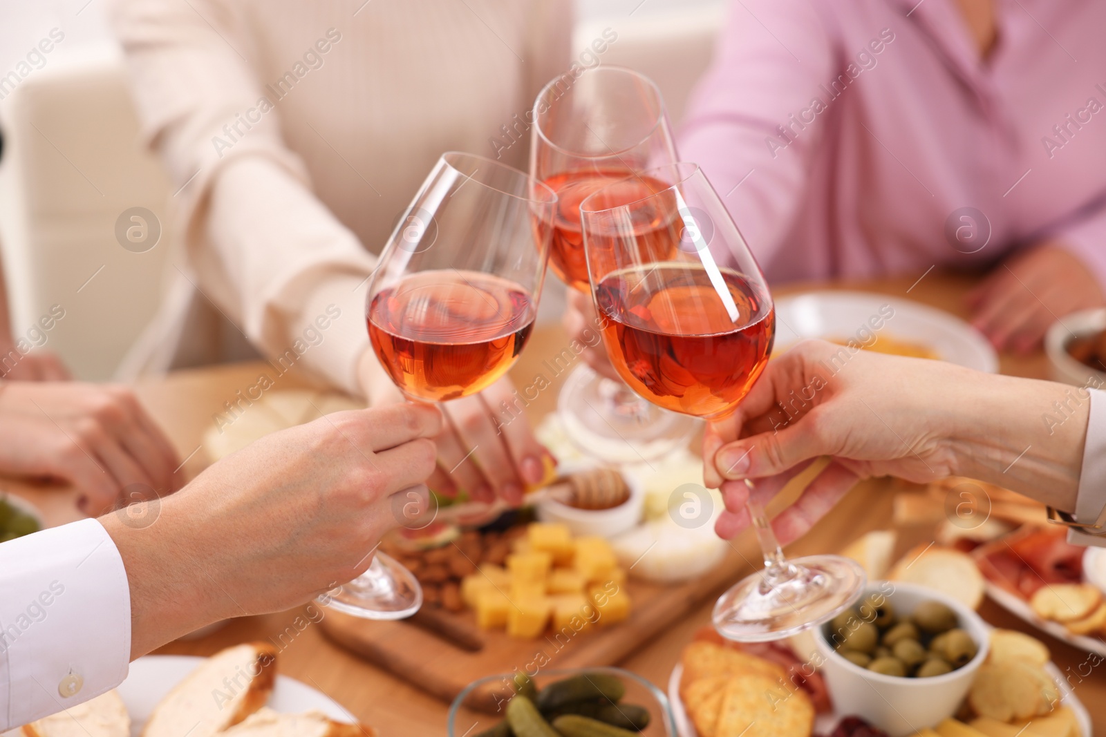 Photo of People clinking glasses with rose wine above table indoors, closeup