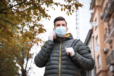 Man in medical face mask and gloves talking on phone while walking outdoors. Personal protection during COVID-19 pandemic