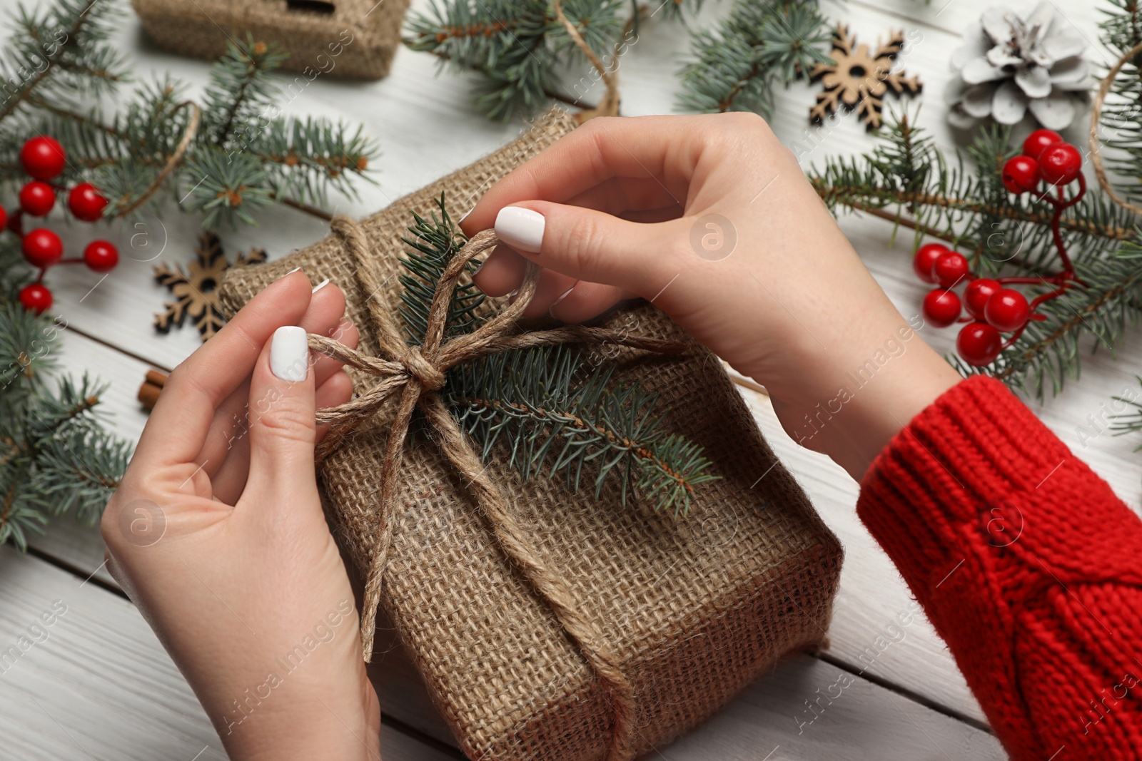 Photo of Woman wrapping Christmas gift at white wooden table, closeup