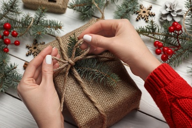 Woman wrapping Christmas gift at white wooden table, closeup