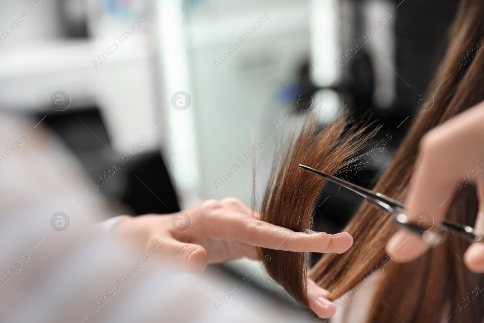 Photo of Hairdresser making stylish haircut with professional scissors in salon, closeup