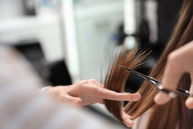 Hairdresser making stylish haircut with professional scissors in salon, closeup