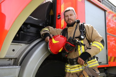 Photo of Firefighter in uniform with helmet near fire truck outdoors