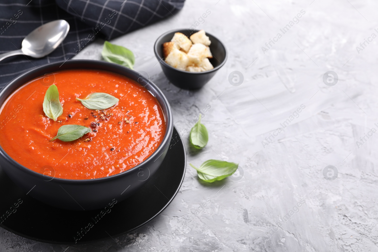 Photo of Delicious tomato cream soup served on grey textured table, closeup. Space for text