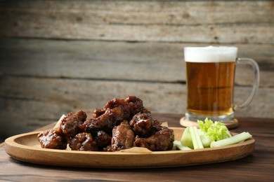 Photo of Delicious chicken wings served with cut celery stalks and beer on wooden table