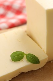 Block of tasty butter with basil on table, closeup