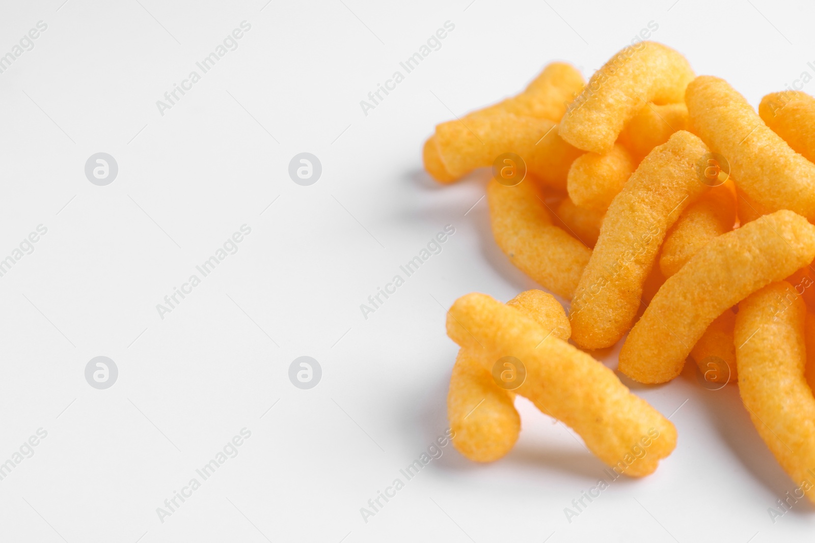 Photo of Heap of tasty cheesy corn puffs on white background, space for text