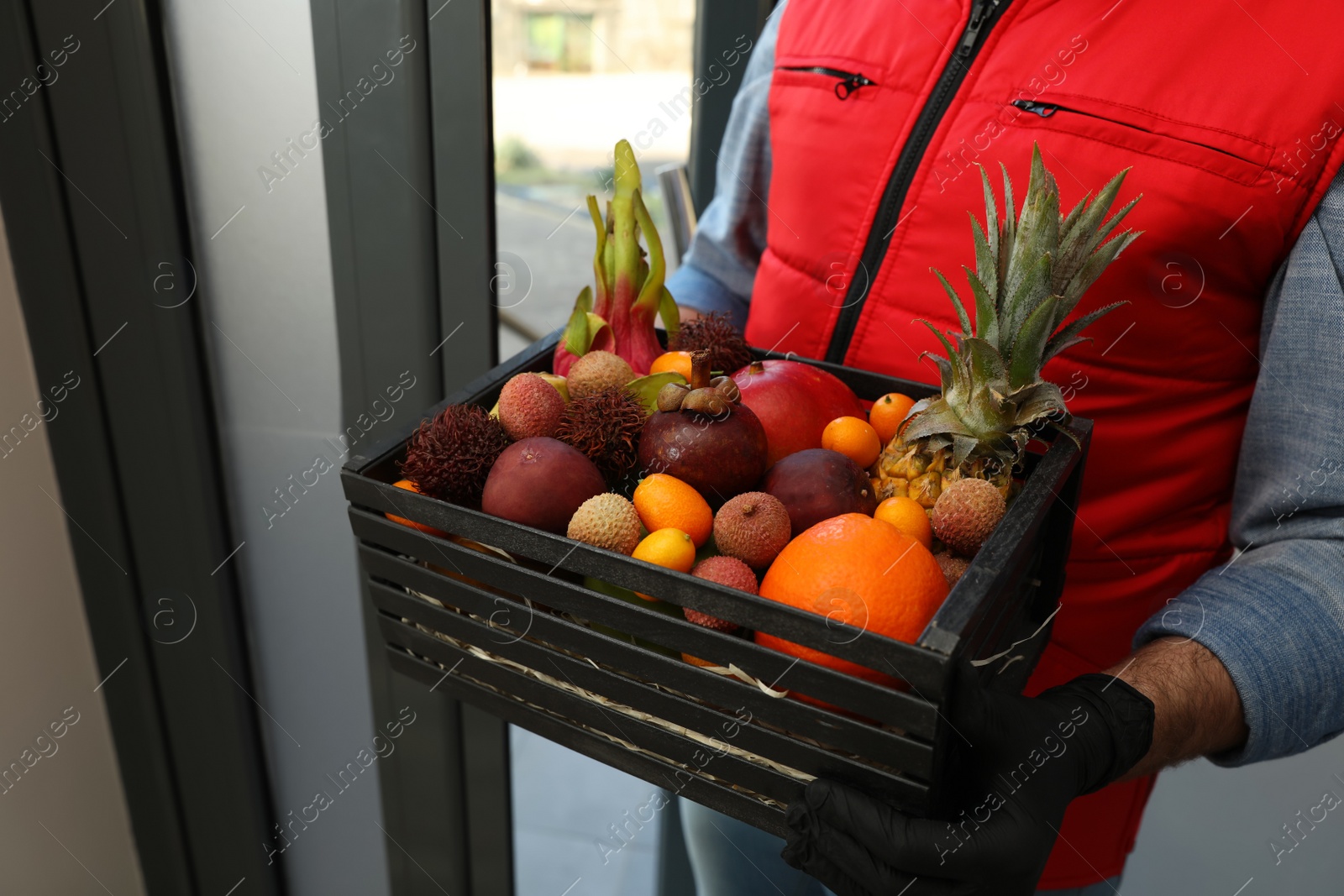 Photo of Courier holding crate with assortment of exotic fruits outdoors, closeup
