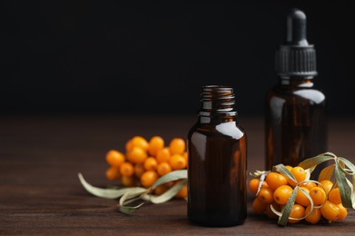 Photo of Natural sea buckthorn oil and fresh berries on wooden table. Space for text