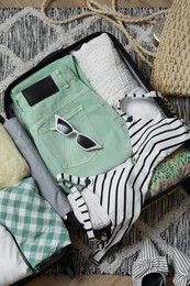 Open suitcase with summer clothes, accessories and shoes on floor, flat lay