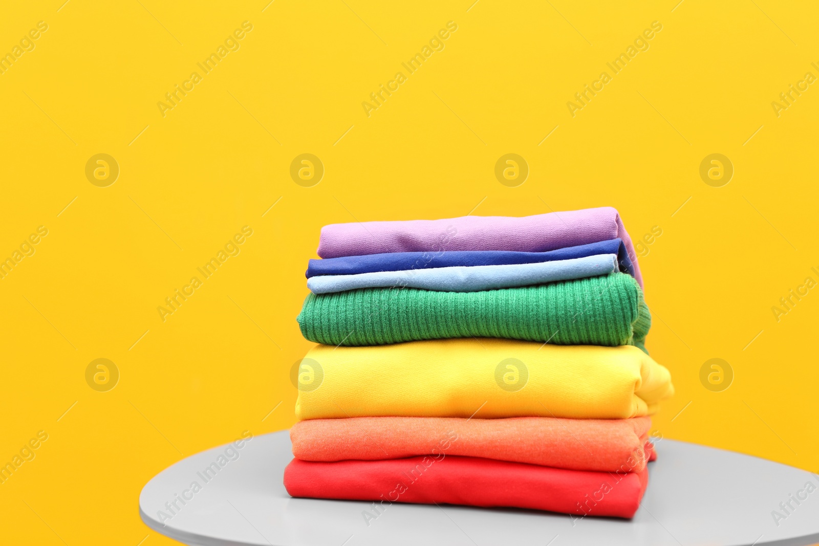 Photo of Stack of rainbow clothes on table against color background