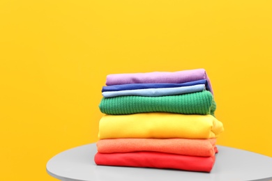 Photo of Stack of rainbow clothes on table against color background