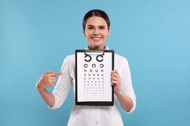 Photo of Ophthalmologist pointing at vision test chart on light blue background