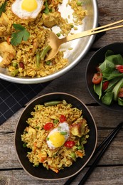 Tasty rice with meat, egg and vegetables in bowl served on wooden table, flat lay