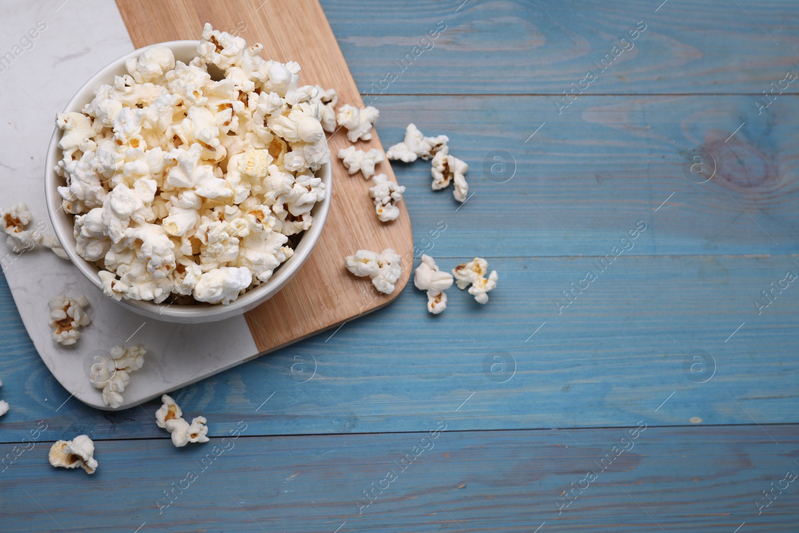 Photo of Tasty popcorn on light blue wooden table, flat lay. Space for text