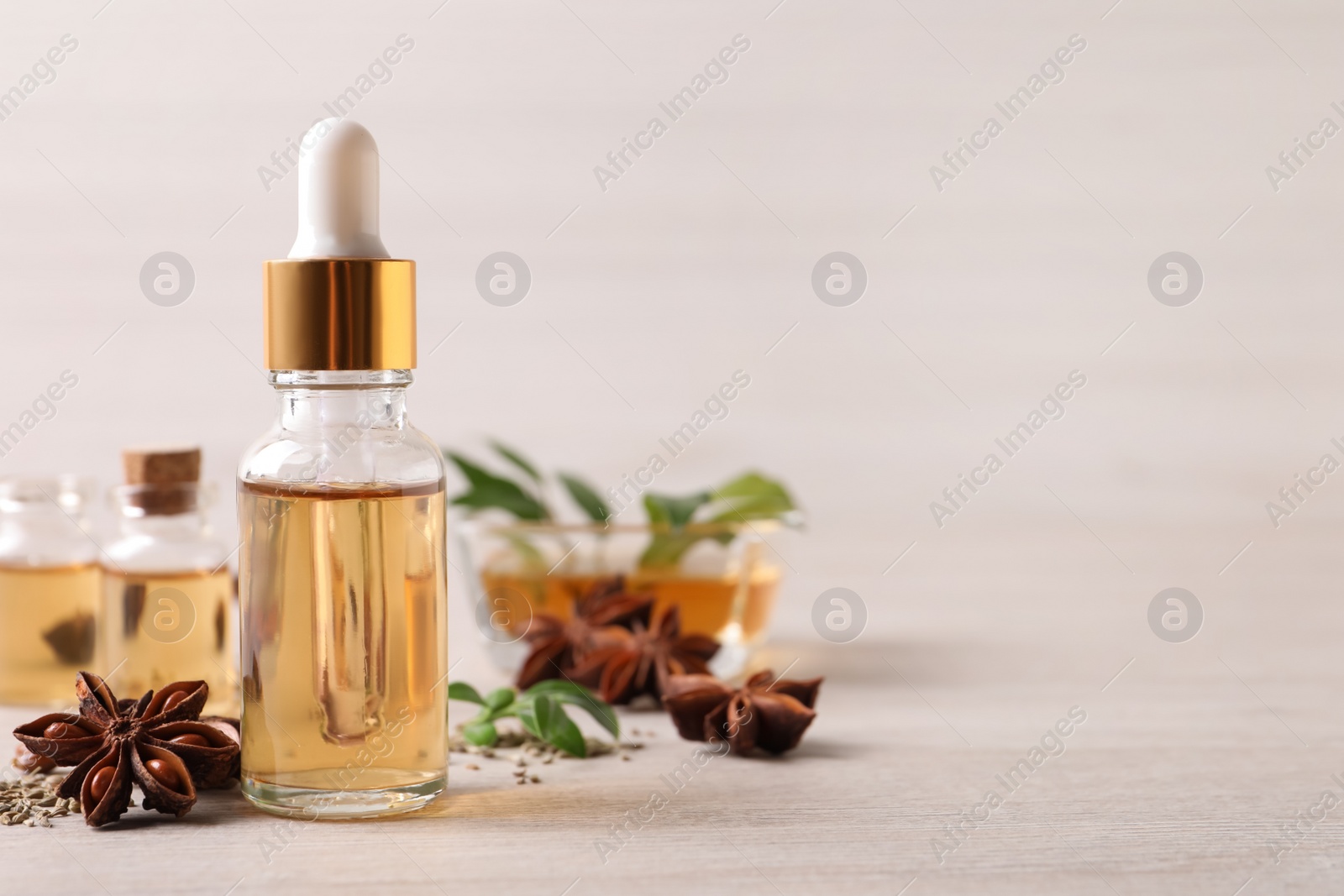 Photo of Bottles of essential oil, anise and seeds on white wooden table. Space for text