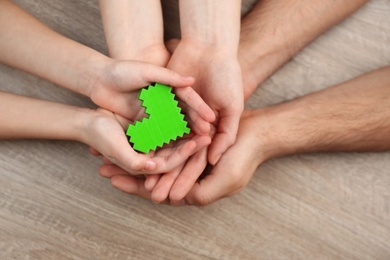 Photo of Parents and kid holding green heart in hands at wooden table, top view. Family day