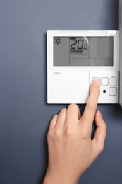 Photo of Woman adjusting thermostat on grey wall, closeup. Heating system