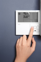 Woman adjusting thermostat on grey wall, closeup. Heating system