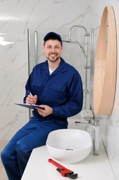 Professional plumber with clipboard checking water tap in bathroom