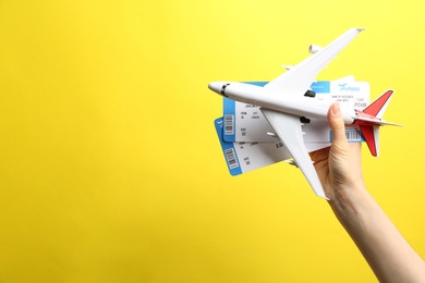 Photo of Woman holding toy airplane and tickets on yellow background, closeup. Space for text