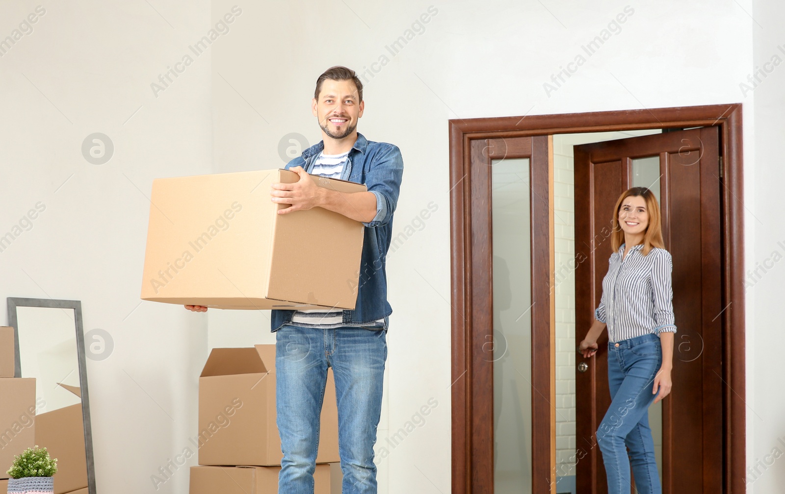 Photo of Couple walking into their new house with moving boxes