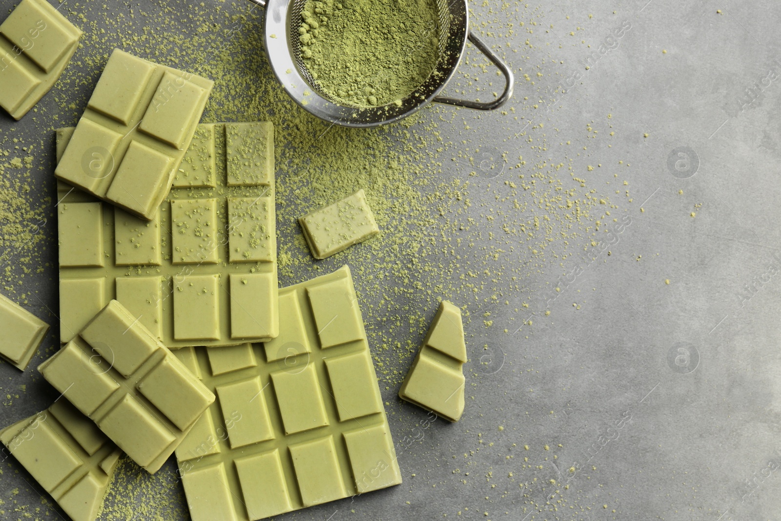 Photo of Pieces of tasty matcha chocolate bars and powder on grey textured table, flat lay. Space for text