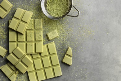 Pieces of tasty matcha chocolate bars and powder on grey textured table, flat lay. Space for text