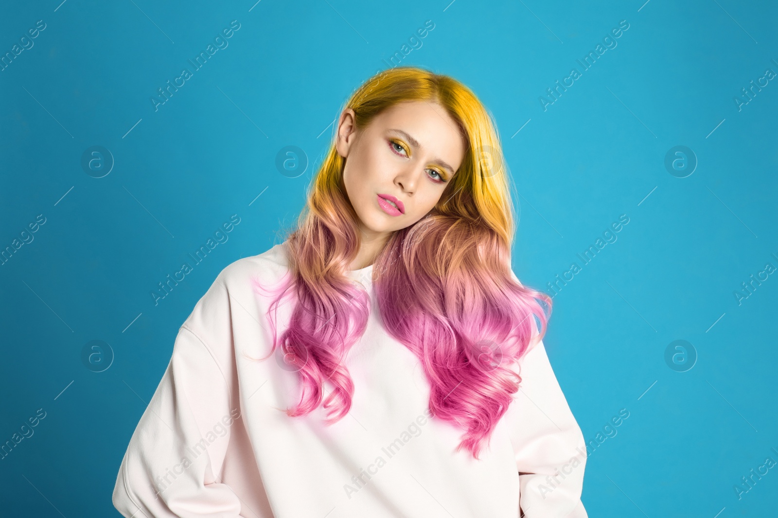 Image of Portrait of young woman with dyed long curly hair on blue background