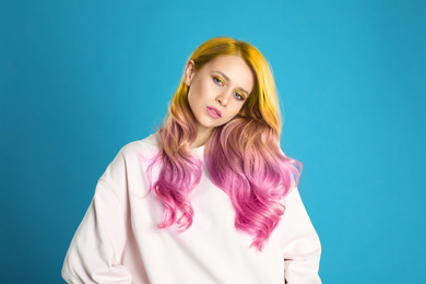 Image of Portrait of young woman with dyed long curly hair on blue background