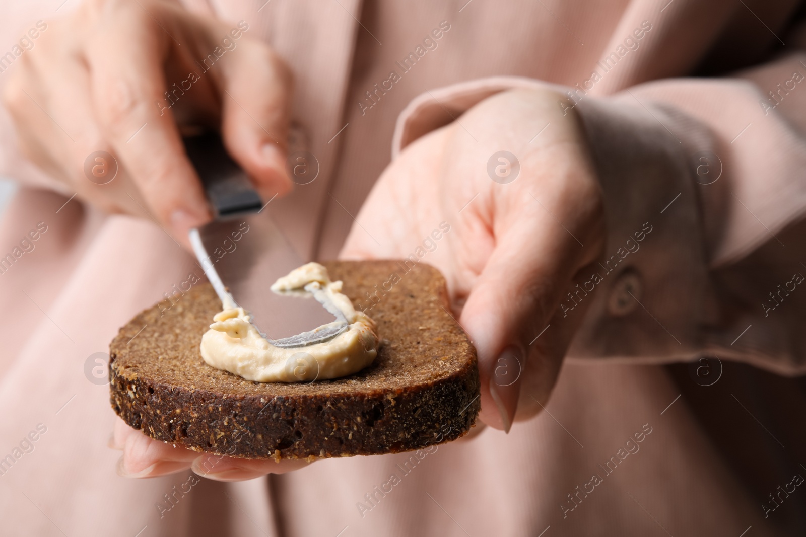 Photo of Woman spreading delicious hummus onto bread, closeup