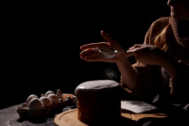 Photo of Young woman making traditional Easter cake at table against black background, closeup. Space for text