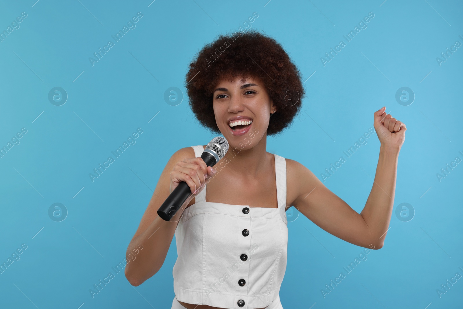 Photo of Curly young woman with microphone singing on light blue background