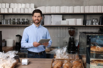 Photo of Happy business owner with tablet at cashier desk in bakery shop