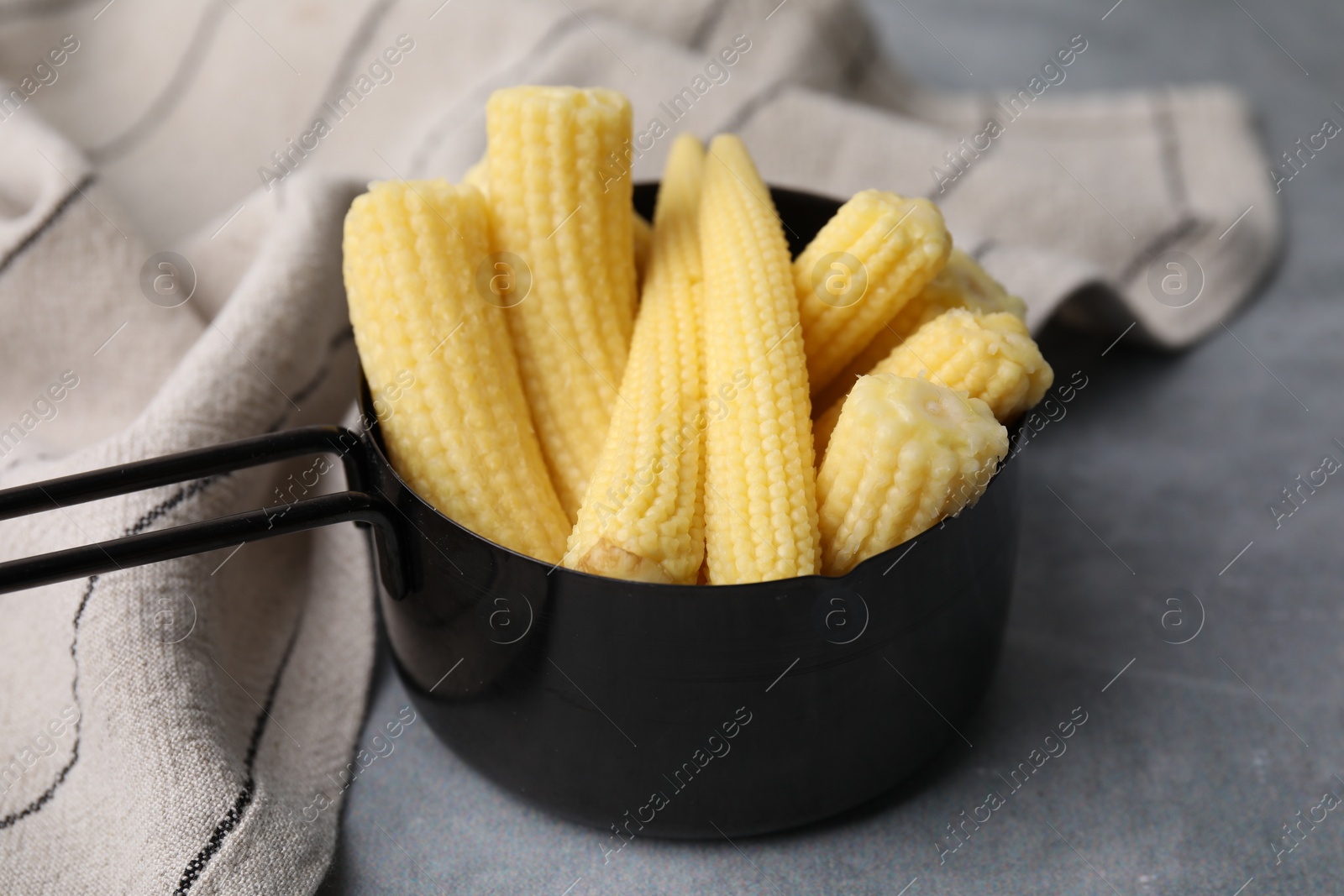 Photo of Tasty fresh yellow baby corns in dish on grey table, closeup