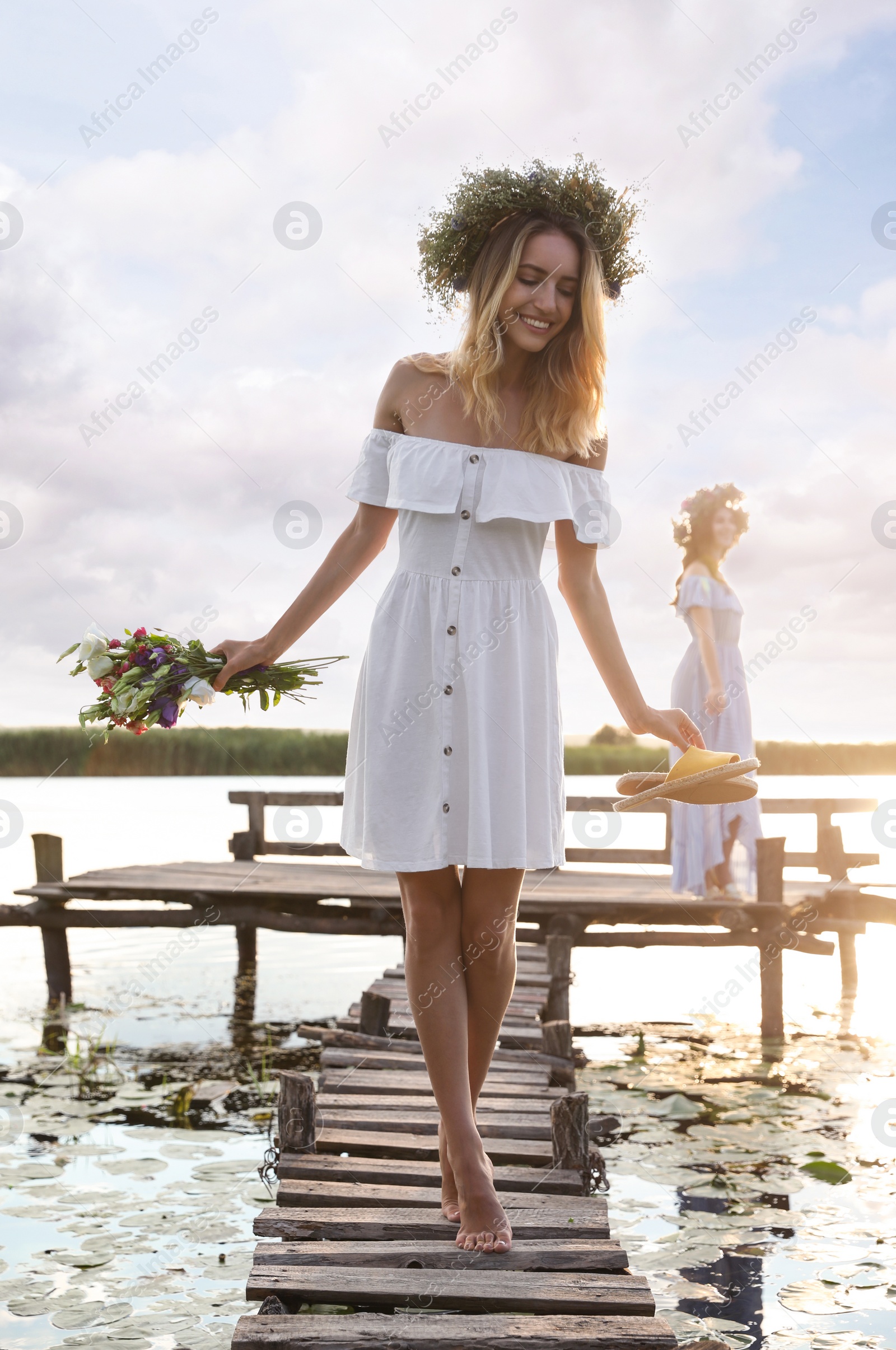 Photo of Young woman wearing wreath made of beautiful flowers on pier near river