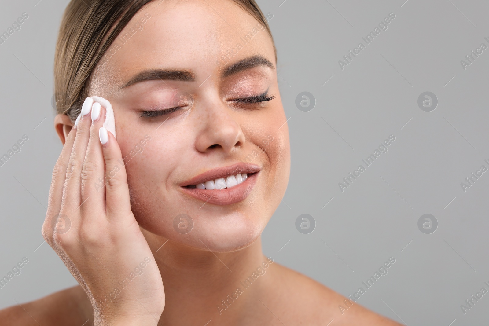 Photo of Beautiful woman removing makeup with cotton pad on grey background, closeup. Space for text