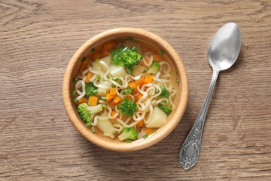 Bowl of fresh homemade vegetable soup served on wooden table, flat lay