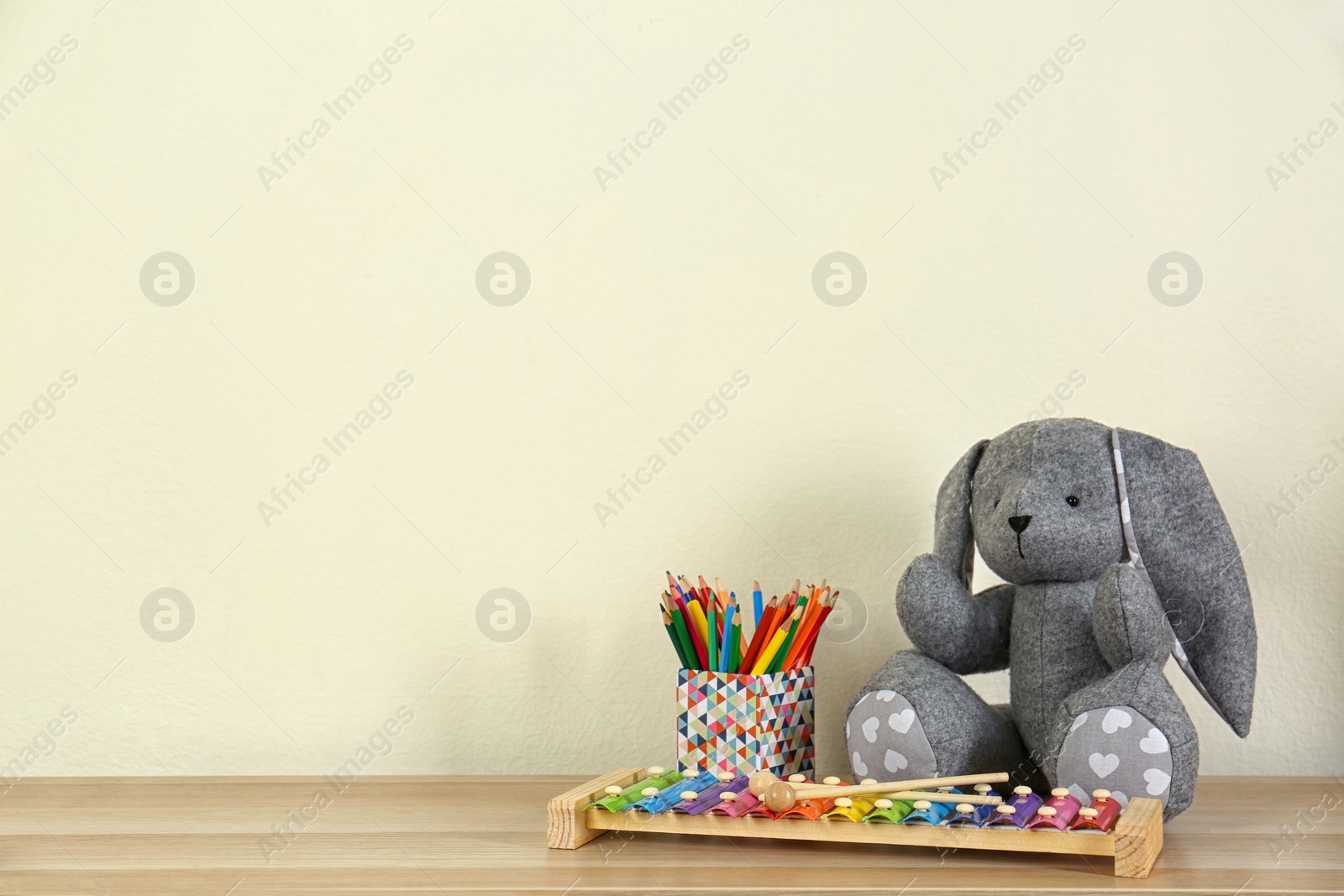 Photo of Toys and holder with color pencils for baby room interior on wooden table near light wall