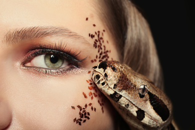 Beautiful woman with boa constrictor on dark background, closeup